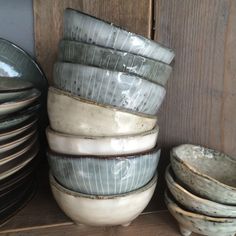 a stack of dishes sitting on top of a wooden shelf next to a pile of plates