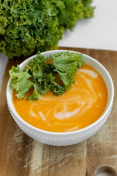 a white bowl filled with carrot soup on top of a wooden cutting board next to a green leafy plant