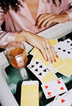 a woman sitting at a table with playing cards and a drink in front of her