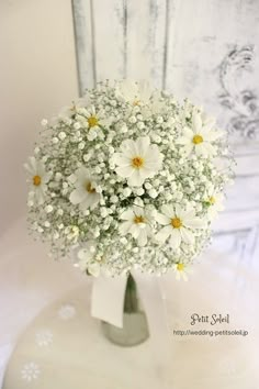 a bouquet of daisies in a vase on a white tablecloth with a chair behind it