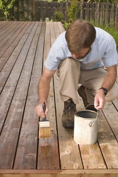 a man painting a wooden deck with a paintbrush