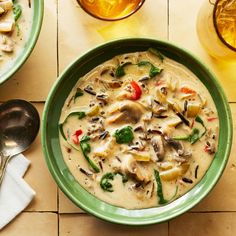 there is a bowl of soup on the table next to two glasses and spoons