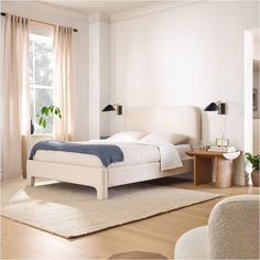 a white bed sitting next to a window on top of a wooden floor in a bedroom