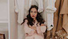 a woman standing in front of a closet with clothes hanging on the rack and holding her arms crossed