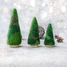 three small green trees sitting next to each other on top of a white surface with pine cones