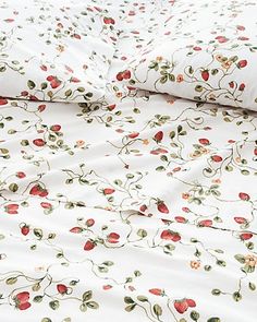 a white bed with red and green flowers on it next to a pillow case that has two pillows