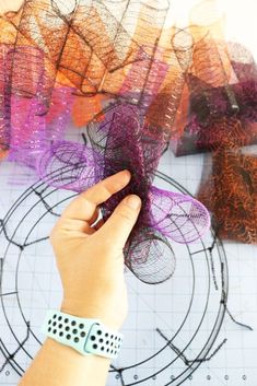 a hand is holding something in front of some colorful mesh pieces on a table with scissors