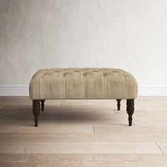 an upholstered bench sits in front of a white wall and hardwood flooring