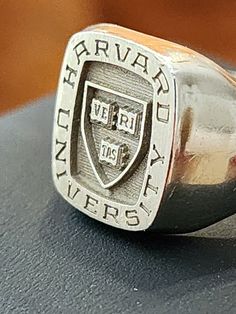 GENUINE HARVARD UNIVERSITY 18K WHITE GOLD SIGNET SCHOOL RING SIZE 9.5 - 10. ITS APPRXIMATELY 11.9 GRAM OF SOLID 18K GOLD. (No stone weight) This is my personal graduate school signet ring from Harvard University, Faculty of Arts and Science. It's Josten brand, 18k solid white gold, and a "hand engraved" signet ring. It is not laser engraved like today's typical ring. In fact, this handmade design was discontinued, and now Josten makes easy laser-engraved signet rings. My name is lightly engraved Arts And Science, School Rings, Signet Rings, Harvard University, Ring Pictures, Graduate School, Handmade Design, Hand Engraving, How To Raise Money