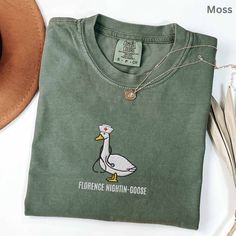 a green t - shirt with a white duck on it and a brown hat next to it