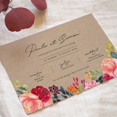 a wedding card with flowers on it sitting next to a leafy plant and some leaves