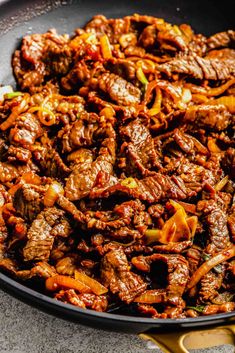 beef and peppers in a skillet ready to be cooked on the stove top with tongs