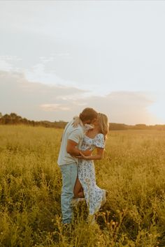 a man and woman are standing in the middle of a field with tall grass at sunset