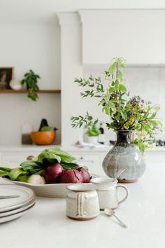 a kitchen counter with plates, bowls and vases filled with vegetables on top of it