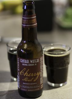 a bottle of beer sitting on top of a table next to two glasses filled with liquid