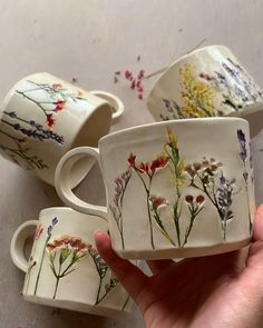 three hand painted mugs with flowers on them are being held in front of the camera