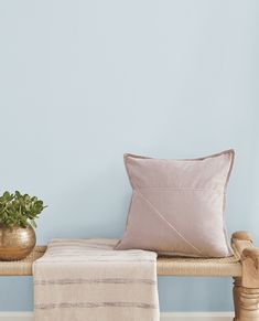 a wooden bench with a pillow on top of it next to a potted plant