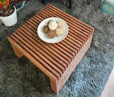 a small wooden table with a white plate on it and some plants in the background