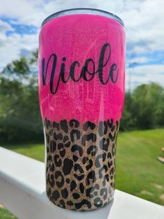 a pink and leopard print tumbler sitting on top of a white fence with the word nicole painted on it