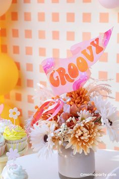 a vase filled with flowers and cupcakes next to a wall decorated with balloons