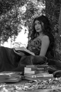 a woman sitting on the ground next to a tree with books in front of her