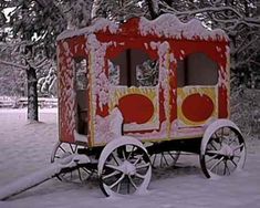 a red and yellow cart sitting in the snow next to some trees with snow on it