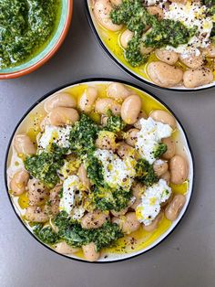 two plates filled with different types of food on top of a gray table next to bowls of pesto and eggs