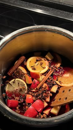 a pot filled with fruit and spices on top of a stove burner next to a wooden spoon