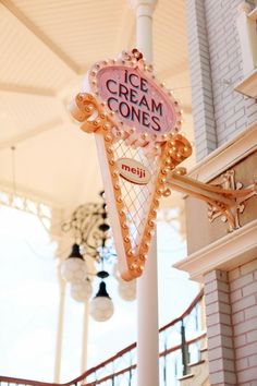 an ice cream cone sign hanging from the side of a white building with lights around it