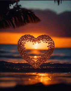 a heart made out of beads sitting on top of the ocean at sunset with palm trees in the background