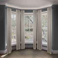 an empty room with three windows and two drapes on the window sill in front of them