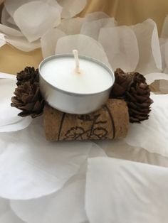 a white candle sitting on top of a piece of cork with pine cones around it