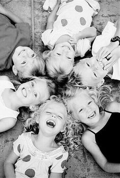 black and white photograph of children laying on the ground with their mouths open, smiling