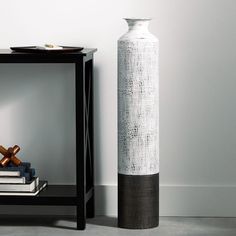 a tall white vase sitting next to a black table with books on top of it