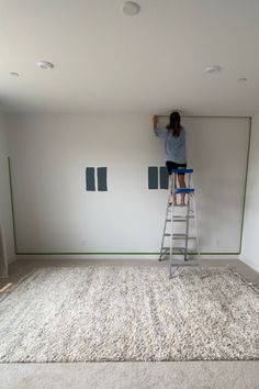 a woman standing on a ladder painting the walls in a room with white carpet and green trim