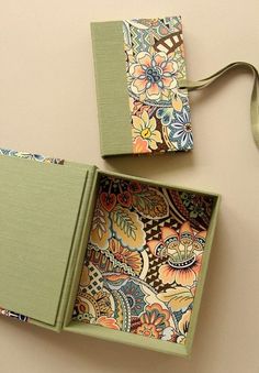 two green boxes with floral designs on them are sitting next to each other and tied together