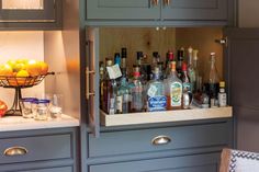 a cabinet filled with lots of bottles and glasses next to a bowl full of oranges