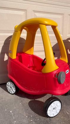 a red and yellow toy car sitting in front of a garage door on the sidewalk