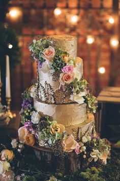 a three tiered wedding cake with flowers on the top is surrounded by greenery and candles