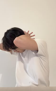 a woman with her hands on her head sitting in front of a white wall and looking at the floor