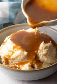 a spoon drizzling gravy over mashed potatoes in a bowl