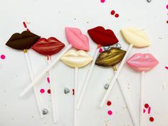 four lollipops with different shapes and colors are on a white surface surrounded by confetti sprinkles