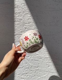 a hand holding a coffee cup with flowers painted on the outside and inside, in front of a white brick wall