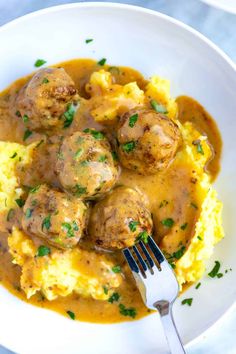 a white bowl filled with mashed potatoes and meatballs covered in gravy