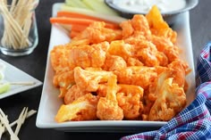 a white plate topped with fried food next to carrots and celery sticks