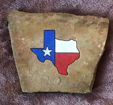 a stone with the shape of texas painted on it, sitting on a brown blanket