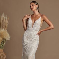 a woman in a white wedding dress standing next to a vase with dried flowers on it