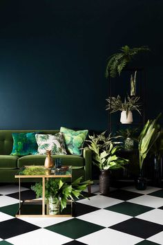 a living room with black and white checkered flooring, green couches, potted plants and paintings on the wall