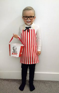 a little boy dressed as a movie character holding a popcorn bucket and wearing glasses, standing in front of a white wall