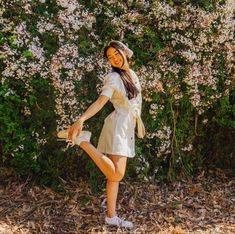 a young woman posing in front of some bushes and flowers with her legs spread out